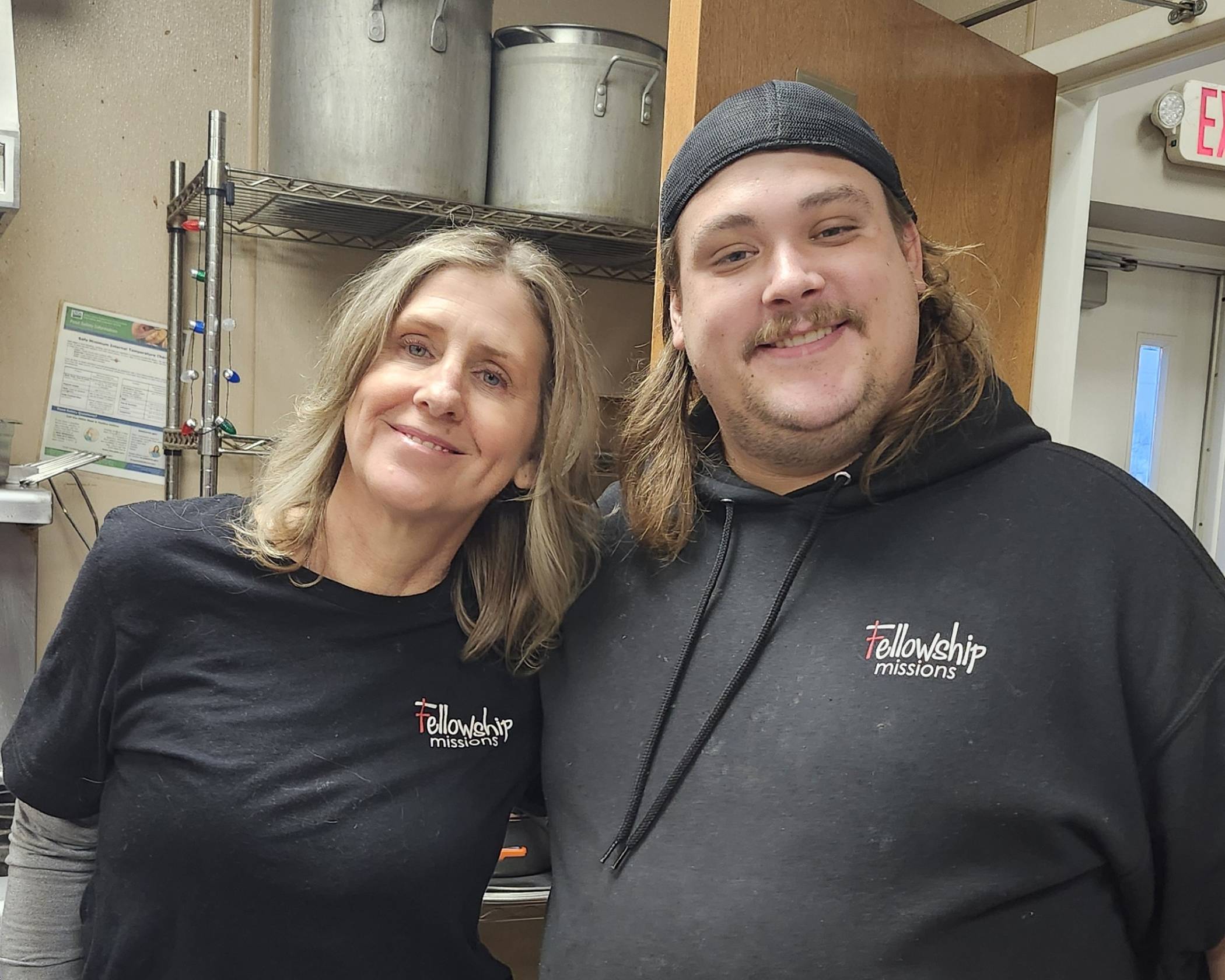 Two people in Fellowship Missions shirts stand together in a kitchen.