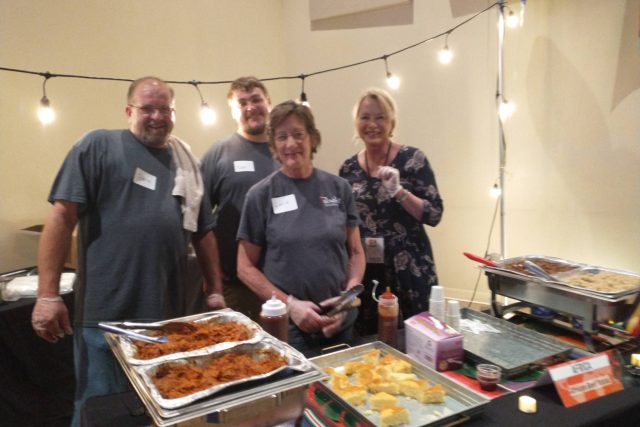 Mechelle and friends stand behind a table with food trays and string lights.